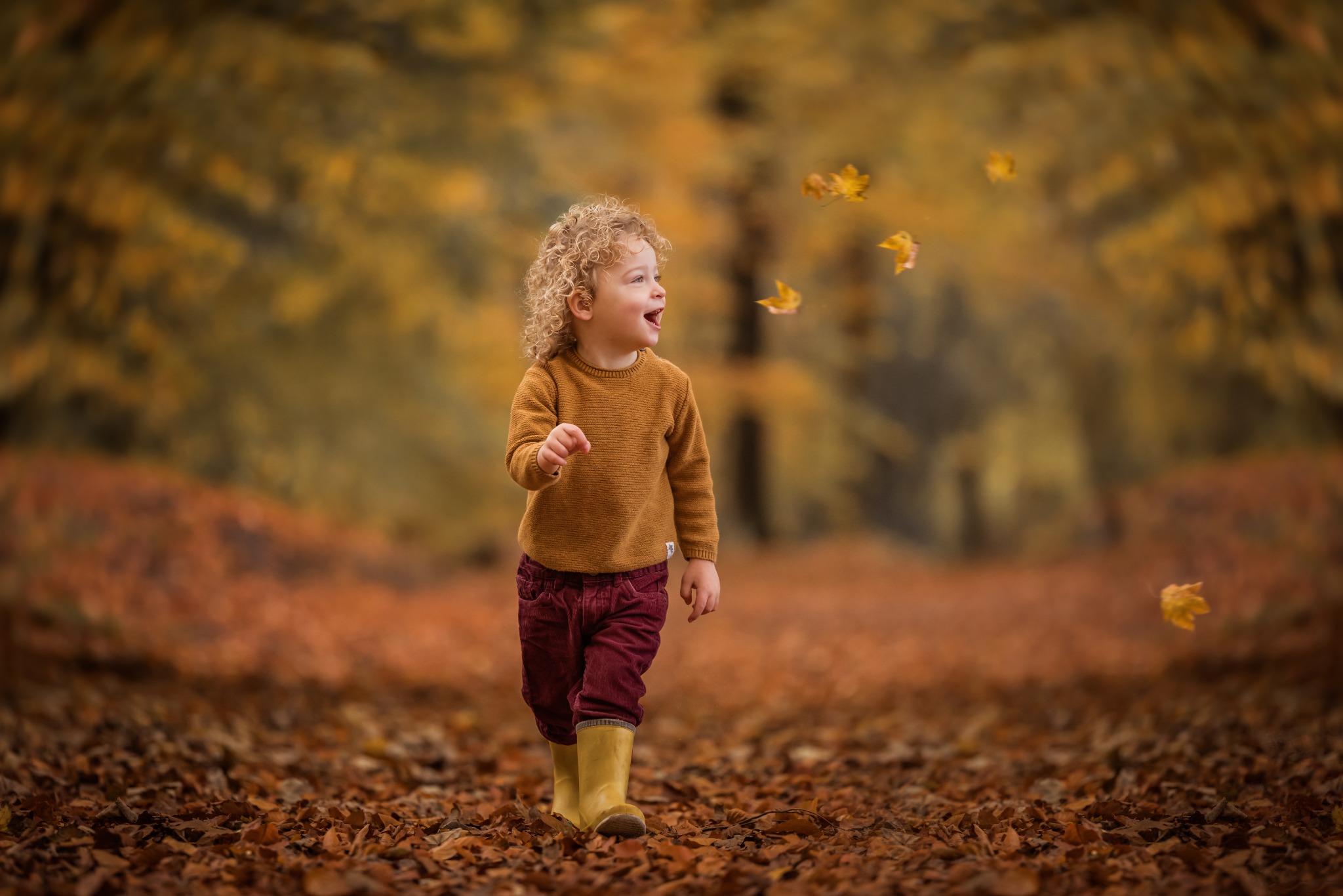 Een kind met gele laarzen tussen dwarrelende bladeren in een herfstbos